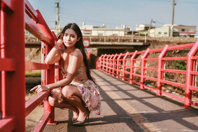 Asian woman in dress crouching on a red bridge