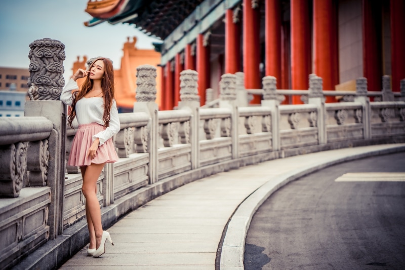 Asian woman in white top and pink skirt posing near a traditional building