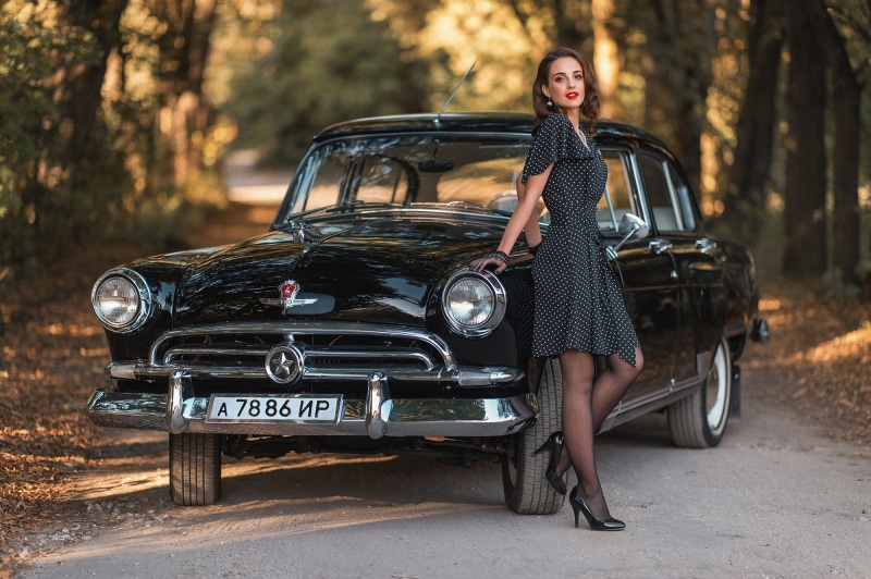 Woman in polka dot dress posing with a vintage Gaz 21 car