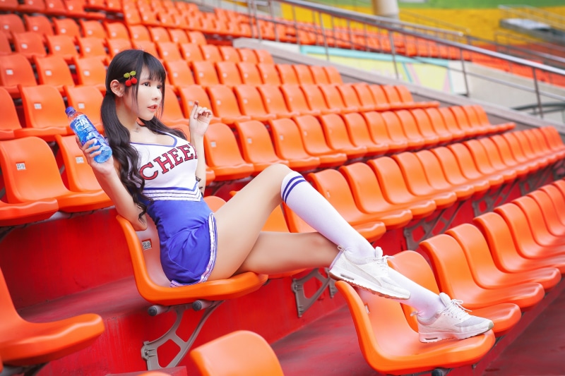Asian cheerleader with bottle sitting in stadium seats