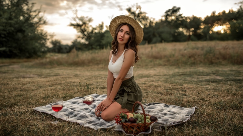 Woman in straw hat having a picnic with wine and fruit