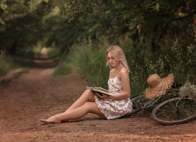 Blonde girl reading a book by a bicycle