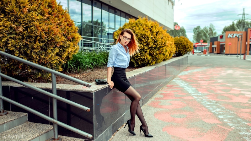 Woman in glasses, blue shirt, and black skirt sitting outdoors