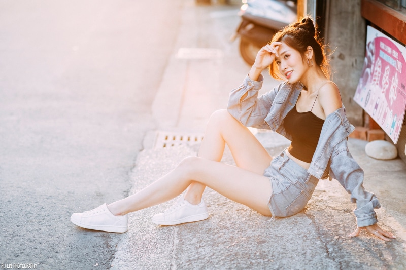 Asian woman in denim shorts and jacket sitting on pavement