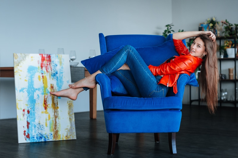 Woman in red jacket and jeans sitting in blue armchair