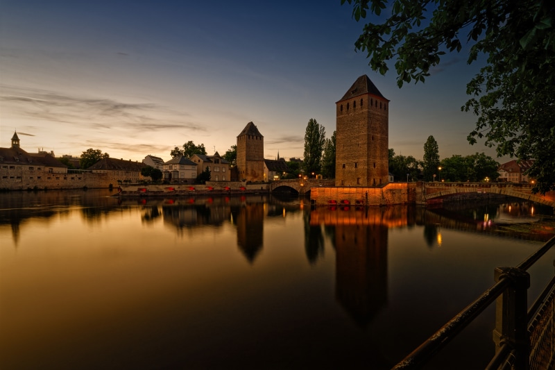 Towers and bridge over river in Strasbourg, France at dusk