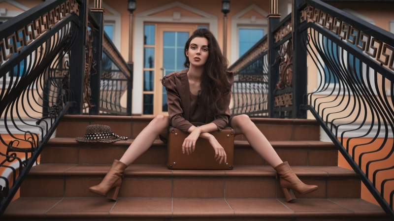 Brunette girl with suitcase and hat on stairs
