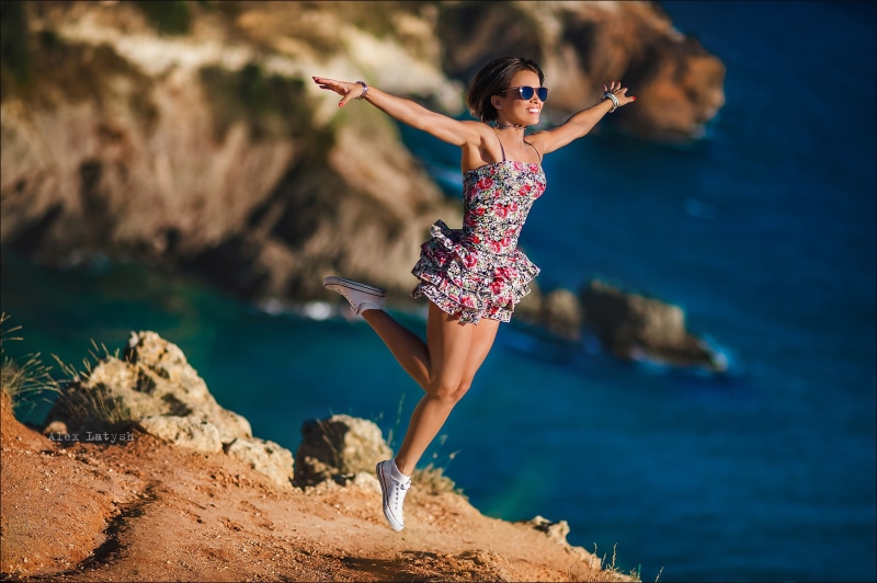 Woman in floral dress jumping by the sea