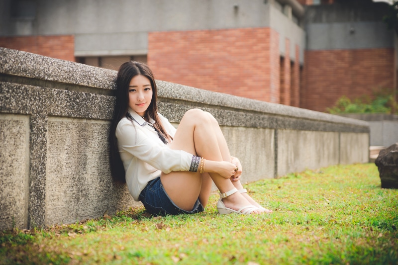 Asian woman sitting on grass near wall