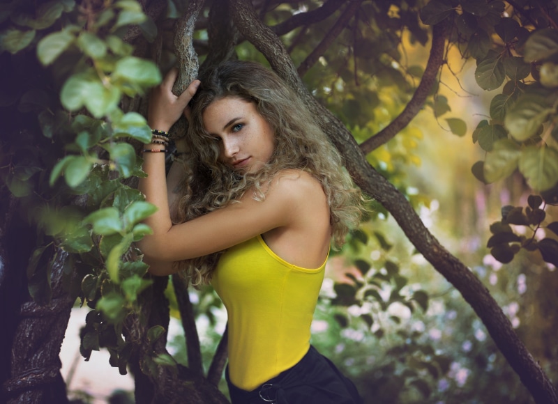 Woman with curly hair in yellow top among trees