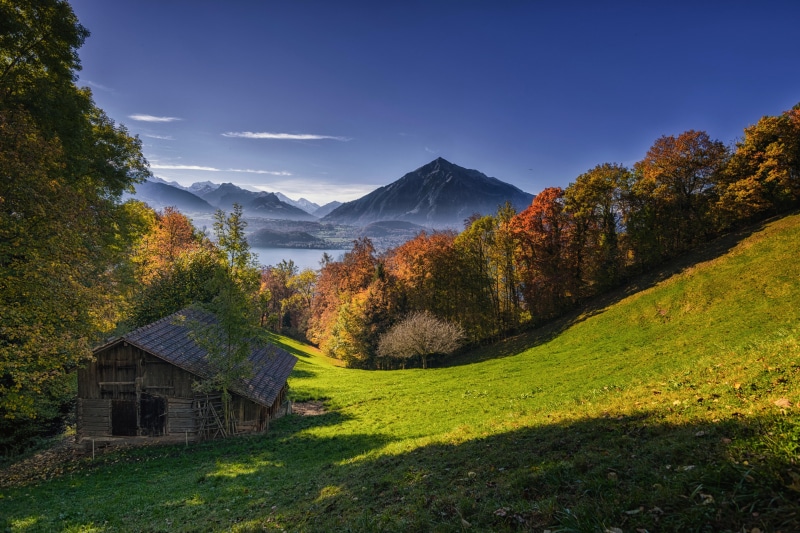 Autumn landscape with a barn, lake, and mountains in Switzerland
