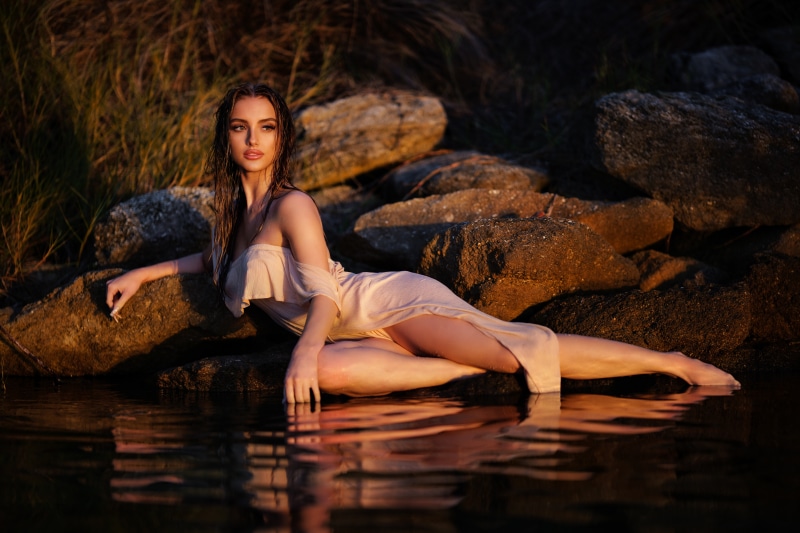 Woman in a dress lying on rocks by the water