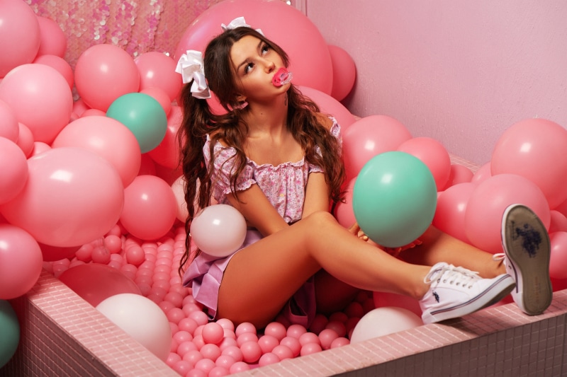 Girl with pacifier in a ball pit with balloons