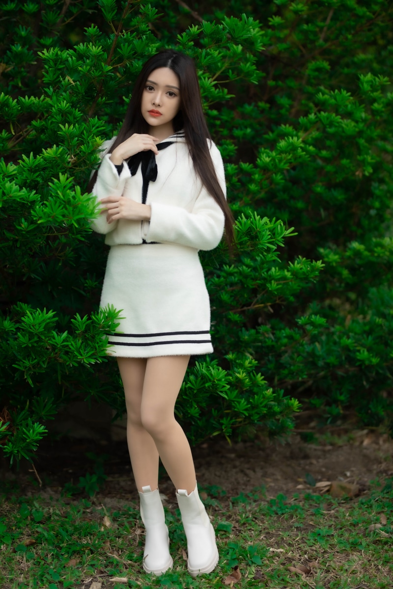 Asian woman in white dress standing near green bushes