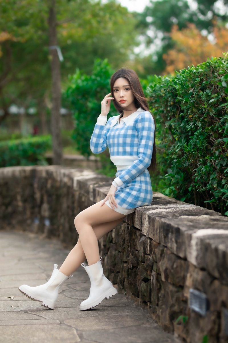 Asian woman in blue checkered dress sitting on stone wall