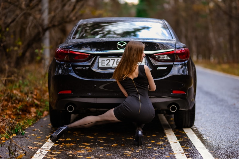 Woman in black dress posing by Mazda 6