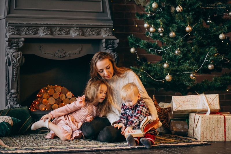 Mother reading to children by Christmas tree and fireplace