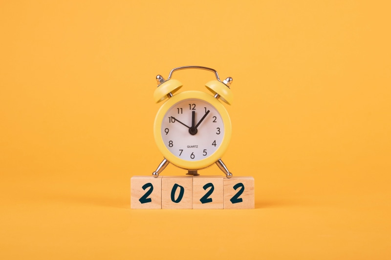 Yellow alarm clock on wooden blocks with 2022