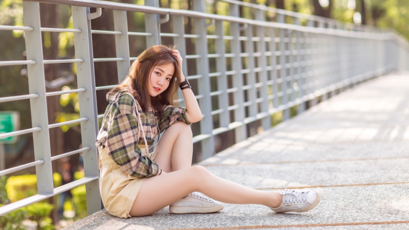 Asian girl with brown hair sitting by a fence