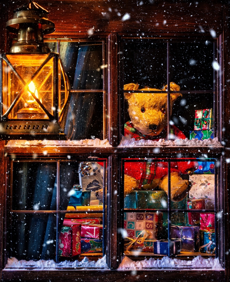 Teddy bear and gifts in a snowy window at Christmas