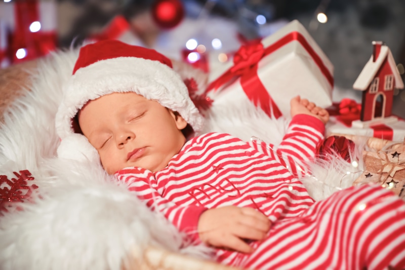 Baby in Santa hat sleeping with Christmas gifts