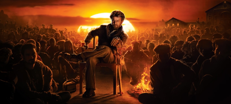 Rajinikanth sitting in front of a crowd at sunset