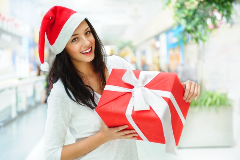 Brunette girl in Santa hat holding a red gift