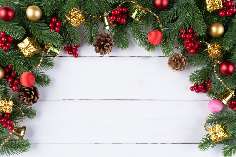 Christmas branches with ornaments and pine cones on white wood
