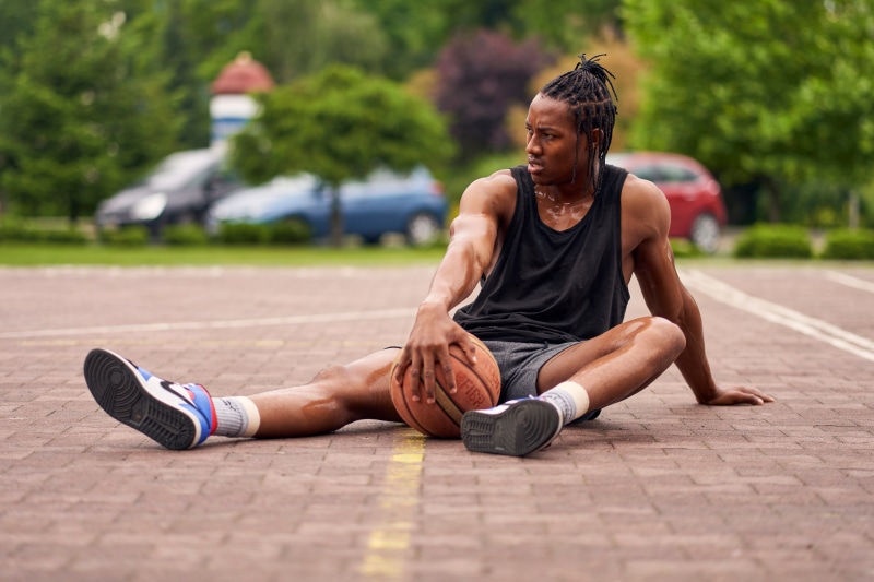 Man in singlet sitting on basketball court with ball