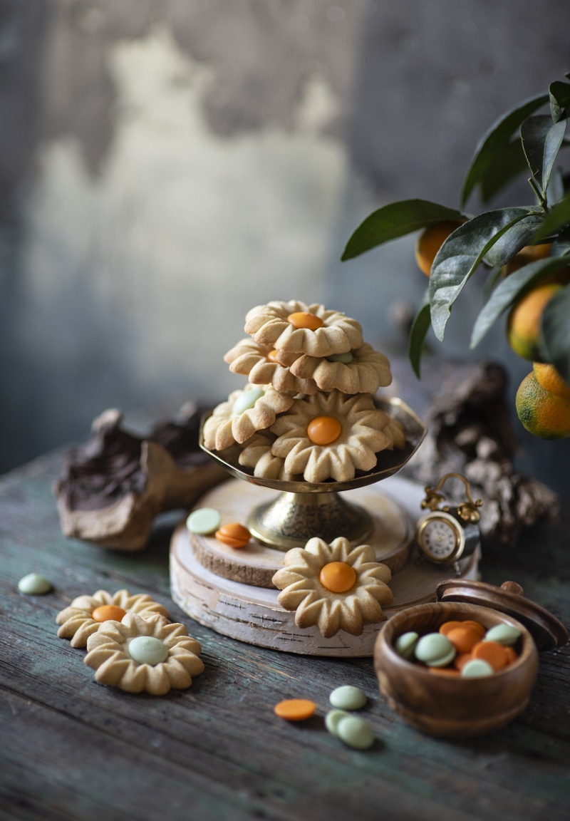 Flower-shaped cookies with orange and mint dragees on wood planks