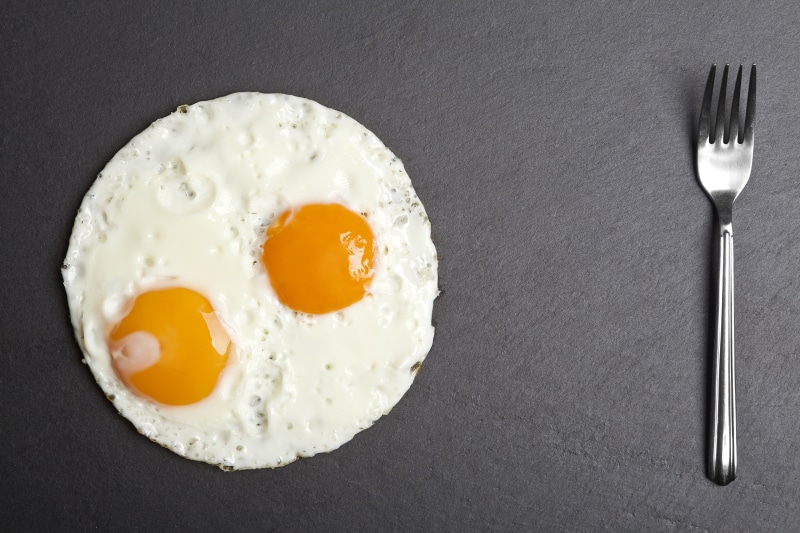 Fried eggs and fork on gray background