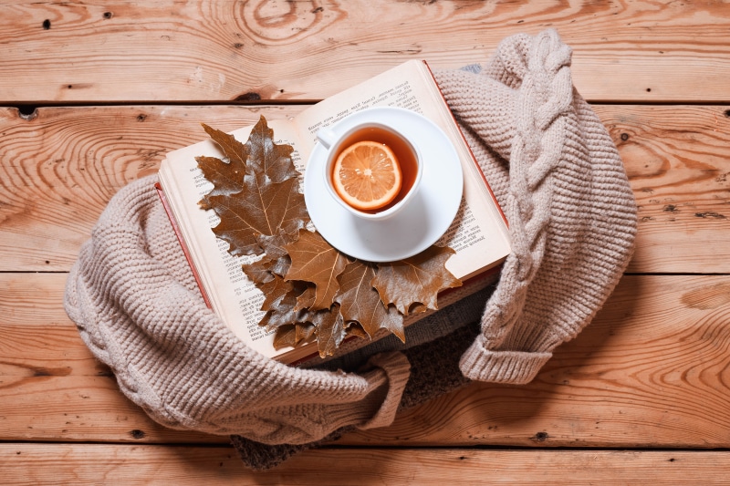 Tea with lemon on an open book with autumn leaves and a sweater