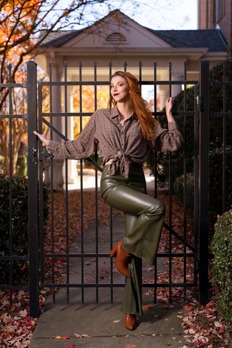 Woman in formal shirt and green trousers posing by a gate