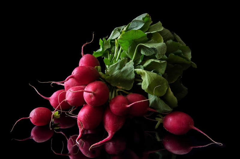 Radishes with green leaves on black background