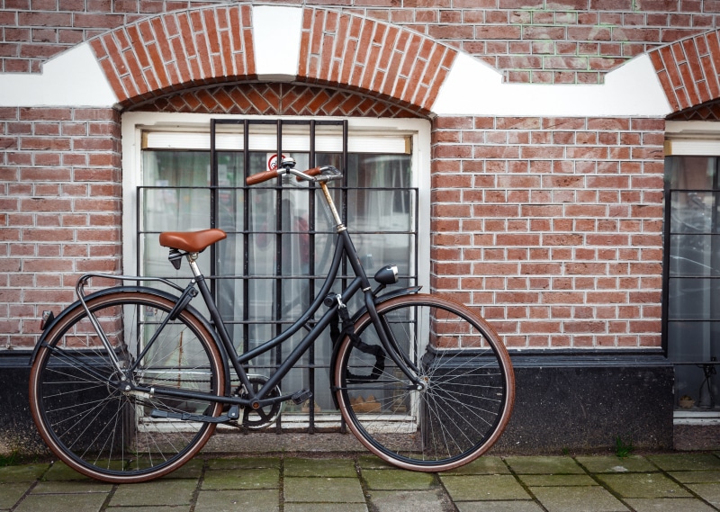 Bicycle parked by a brick wall and window