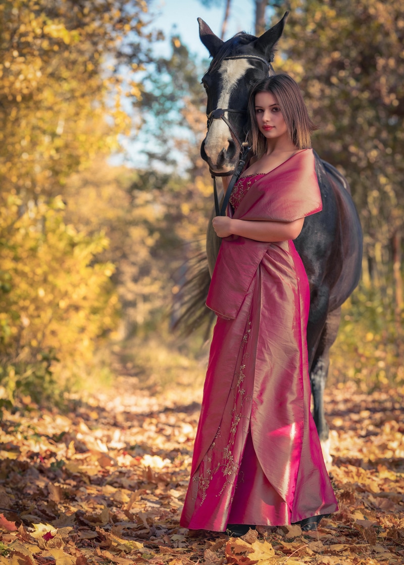 Woman in a pink dress with a horse in autumn