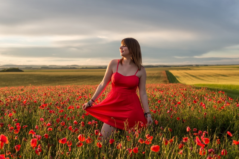 Woman in red dress in poppy field at sunset