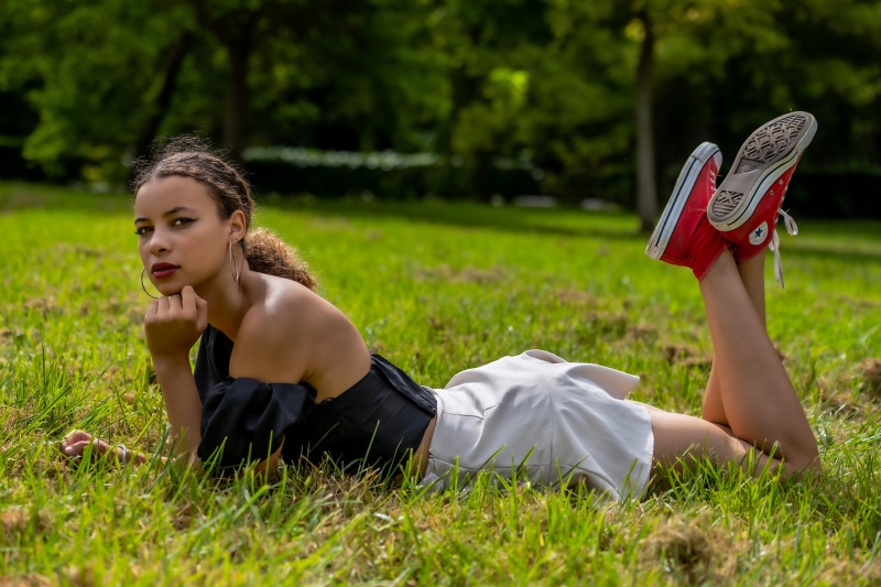 Woman in skirt and red sneakers lying on grass