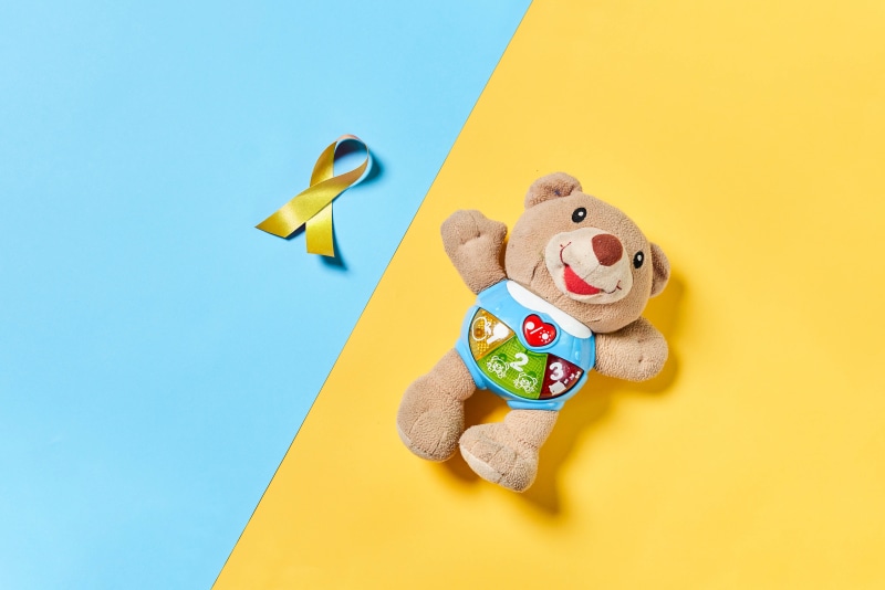 Teddy bear and yellow ribbon on colored background