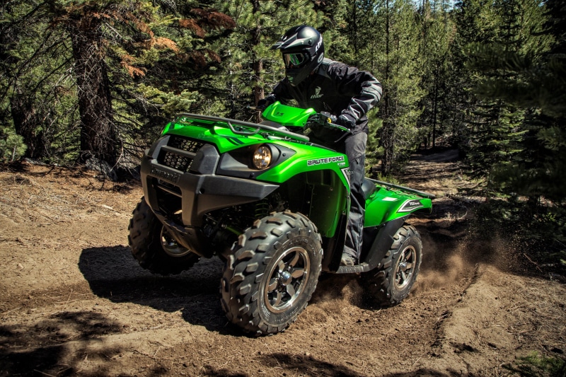 Man riding a green Kawasaki Brute Force ATV on a forest trail