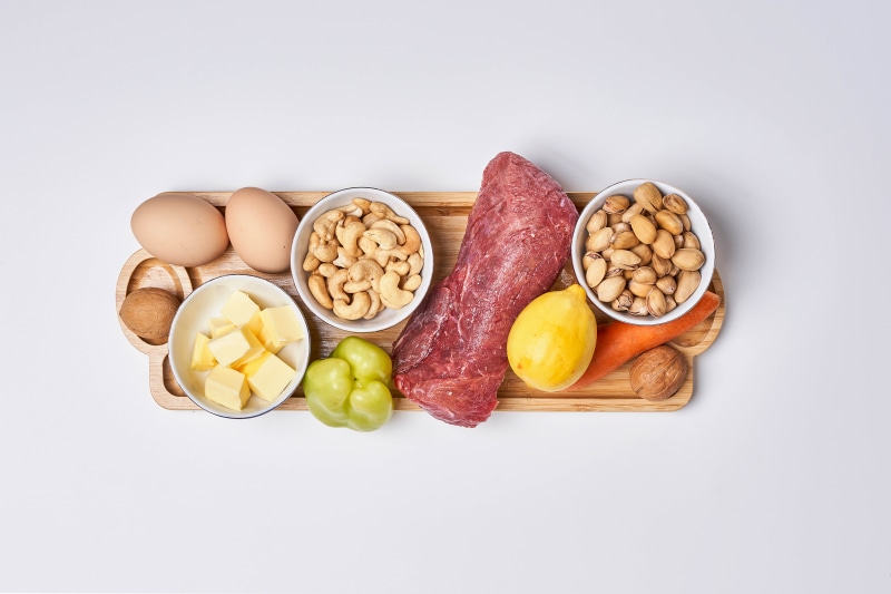 Meat, eggs, nuts, butter, lemon, and vegetables on a cutting board