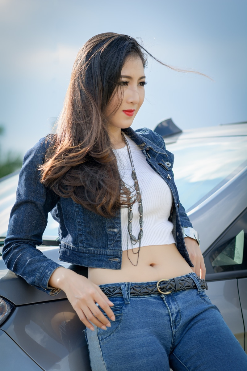 Brunette girl in denim jacket and jeans leaning on car