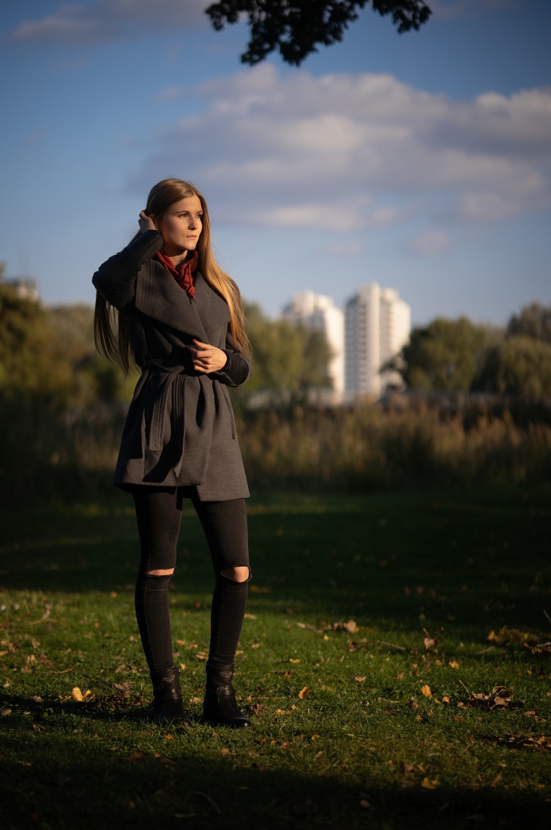 Woman in coat and ripped jeans in autumn park