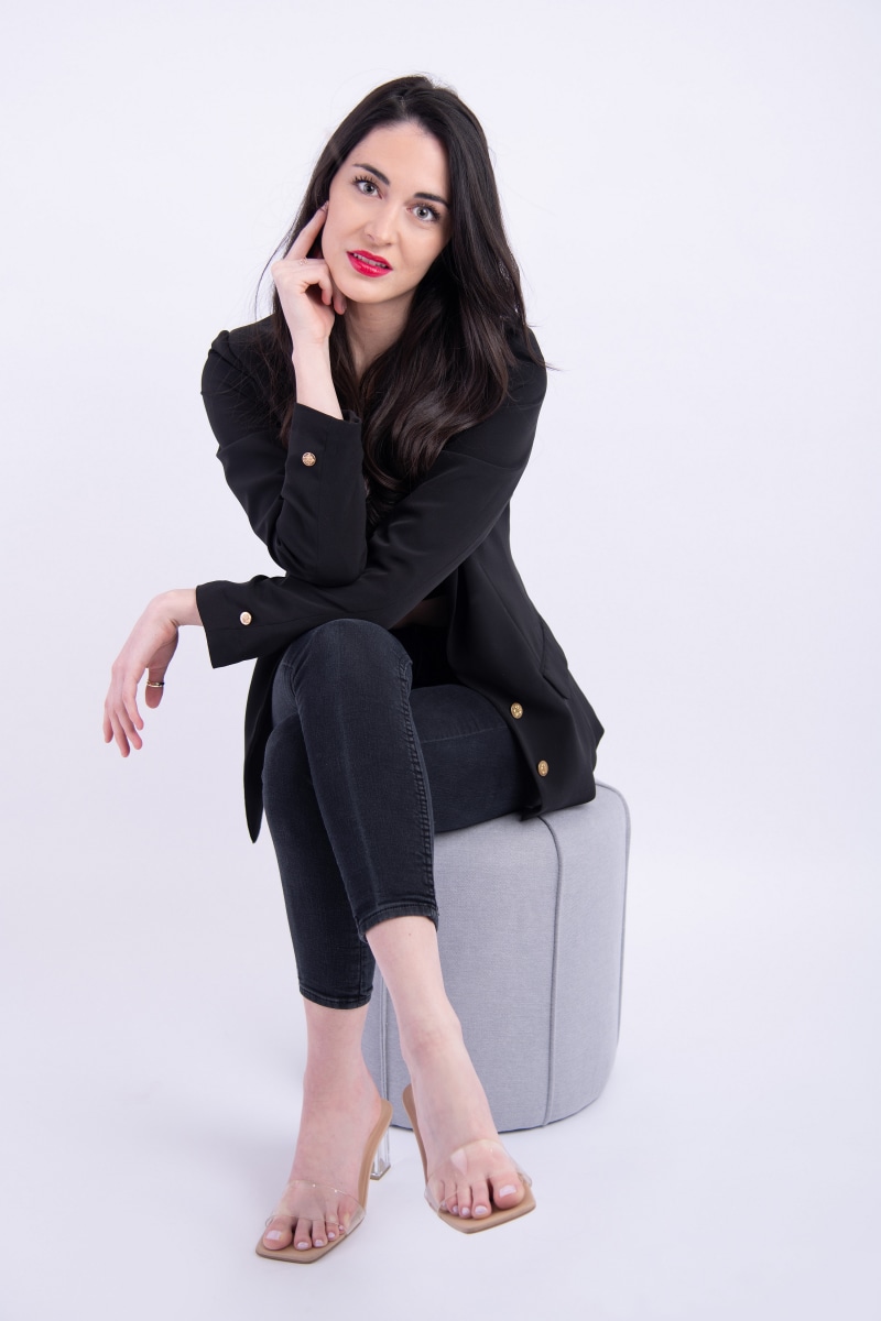 Brunette woman in black suit jacket sitting on stool