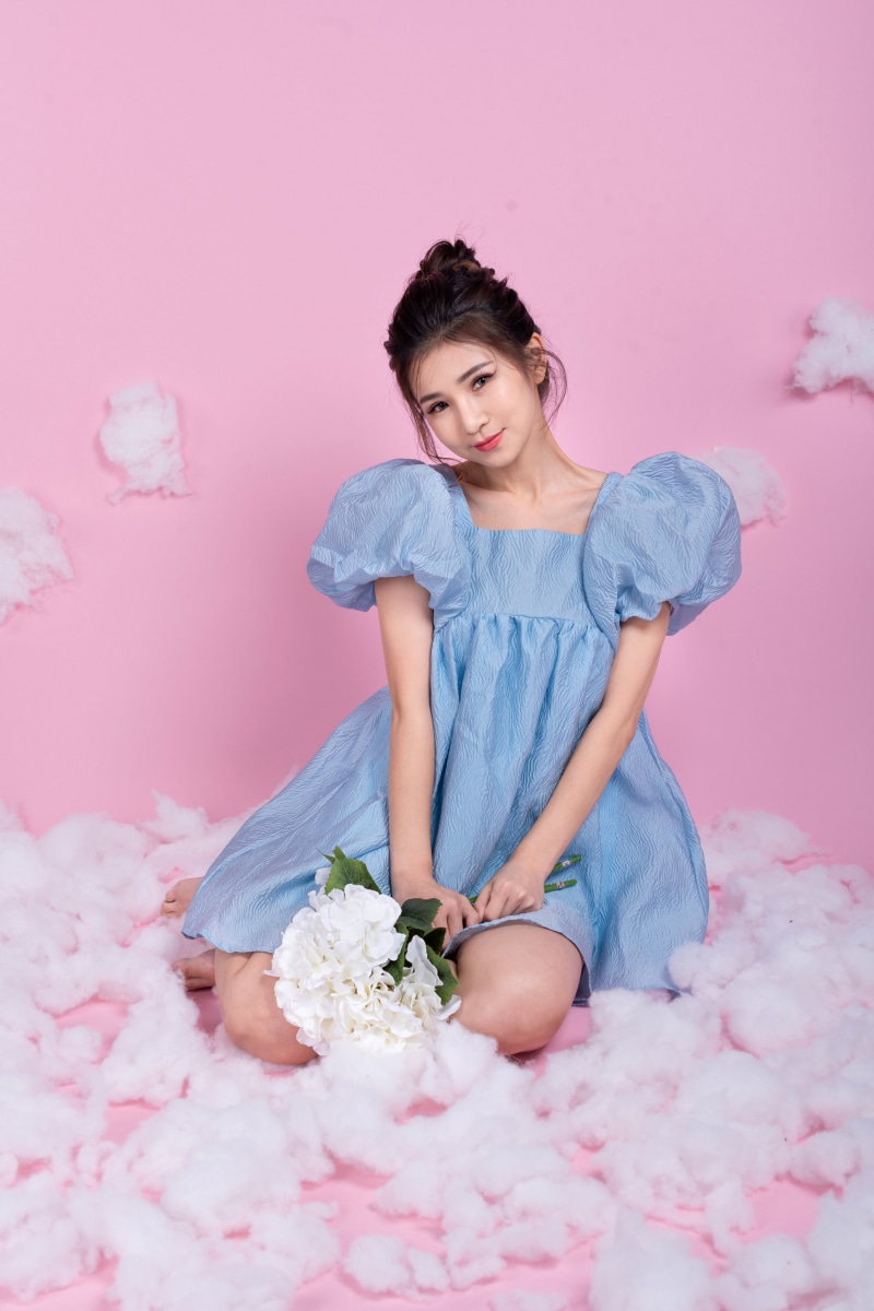 Asian woman in blue dress holding white flowers on pink background