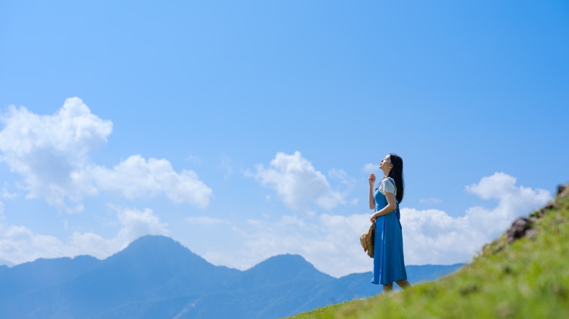 Asian woman in blue dress on grassy hill under blue sky