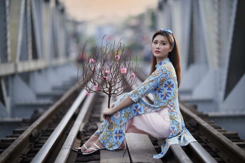 Asian woman in traditional dress on train tracks with branches