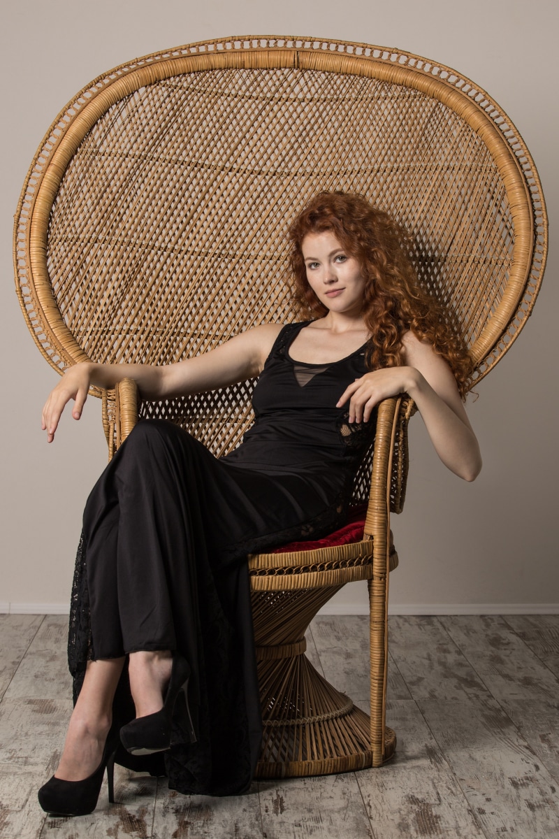 Heidi Romanova sitting in a wicker peacock chair