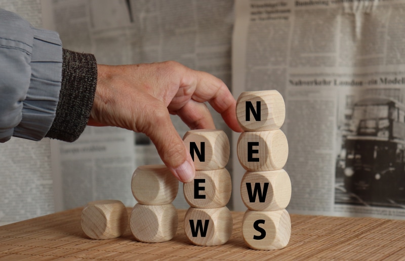 Hand stacking wooden blocks spelling NEWS