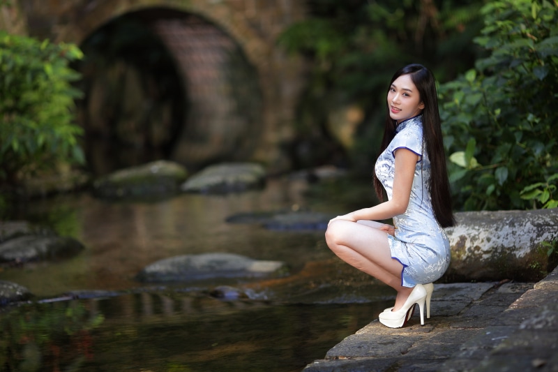 Asian woman in a light blue dress posing by a stream